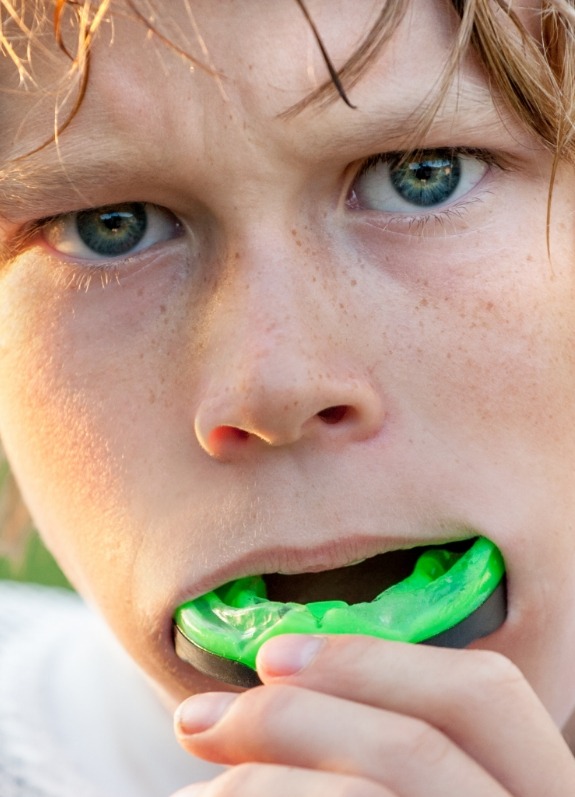 Young boy putting green athletic mouthguard into his mouth