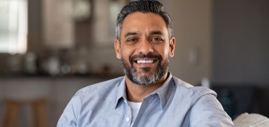 Man in light blue collared shirt smiling on couch