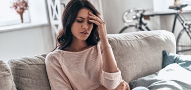 Woman sitting on couch and touching her forehead with pained expression