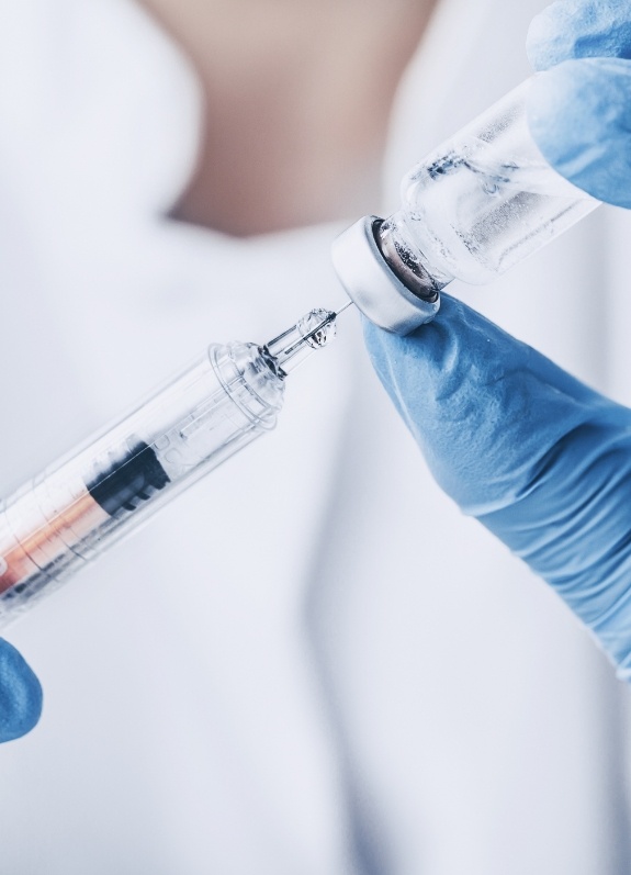 Person drawing syringe from vial of clear liquid