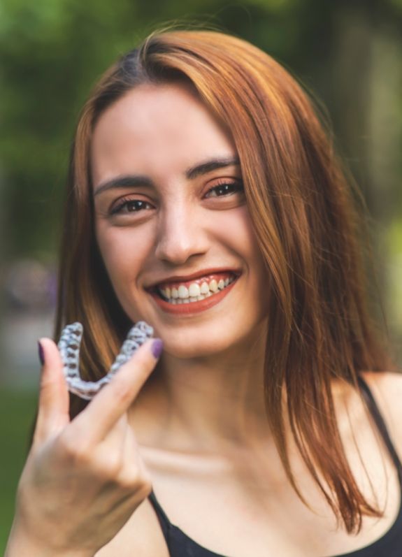 Smiling woman holding an Invisalign tray outdoors
