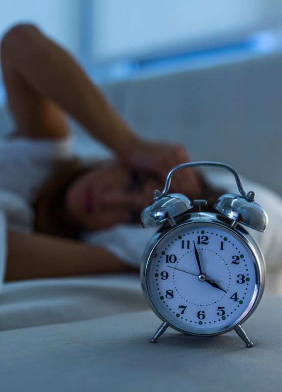 Woman laying awake in bed while bedside clock reads four A M