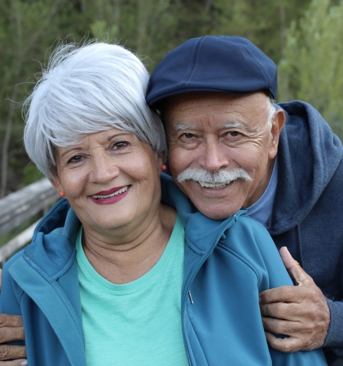Senior couple hugging and smiling outdoors after restorative dentistry in Jonesboro