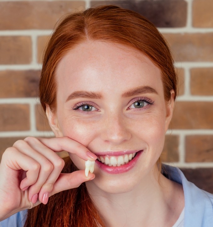 Smiling woman holding a tooth after tooth extraction in Jonesboro